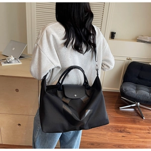 Detailed view of black nylon travel tote featuring leather handles and metal hardware