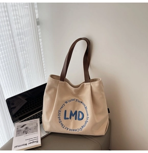Detail of embroidered LMD logo and brown leather handles on canvas tote bag