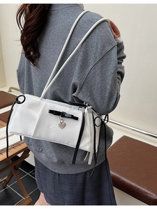 White minimalist shoulder bag with black bow and heart pendant on model's shoulder