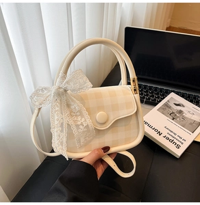 Detailed shot of beige plaid handbag featuring a delicate lace bow and circular buckle