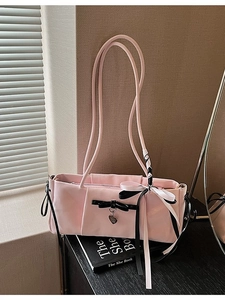 Elegant pink rectangular shoulder bag with ribbon bow and heart pendant on a book