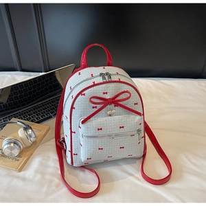 Detail view of mini cream backpack with red bow prints and heart pendant in a cozy setting