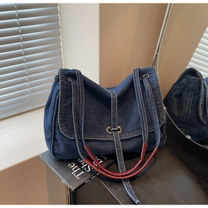 Close-up of denim shoulder bag with silver lock and burgundy handles on a dark surface