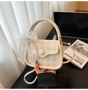 Close-up of cream leather handbag with plaid flap and lace bow detail in hand