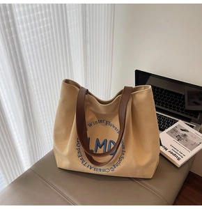 Detail view of khaki canvas tote bag featuring LMD embroidery and brown leather straps