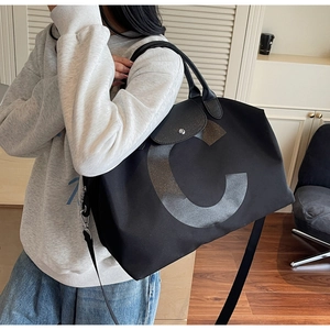 Detail of black travel tote bag with large letter C design and leather top handles
