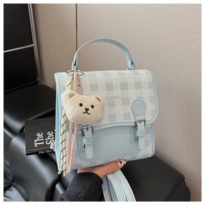 Gros plan d'un mini sac à dos à carreaux bleu clair avec breloque d'ours en peluche