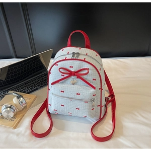 Detail view of white plaid backpack with red bow print and heart metal pendant