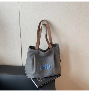 Detailed embroidery on grey canvas tote bag with brown leather straps and blue lettering