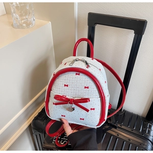Close-up of mini white backpack featuring red bow pattern and glossy heart pendant