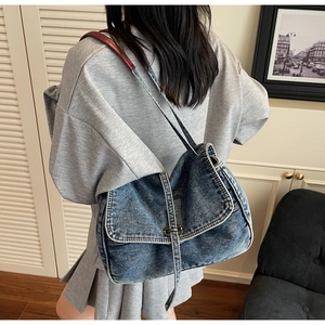 Détail d'un sac en jean vintage avec bandoulière en cuir rouge sur l'épaule
