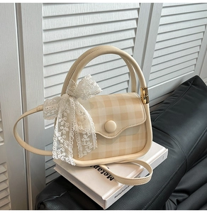 Detail of light beige checkered handbag with lace bow and thin leather strap on books