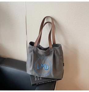 Detail of dark grey canvas tote bag with brown leather handles and blue embroidery