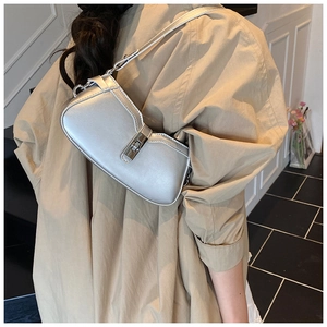 Silver metallic baguette bag with twist lock closure worn on shoulder by model