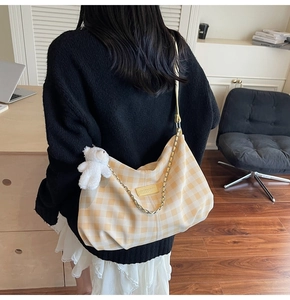Detailed view of yellow gingham canvas tote bag with plush bear charm and chain strap