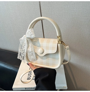 Detail of a beige crossbody bag featuring yellow plaid flap and a white lace bow charm