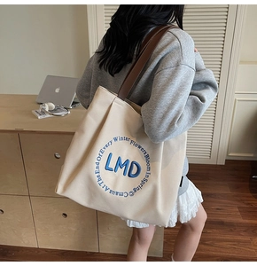 Detailed view of the embroidered LMD logo and quote on a canvas tote bag's front