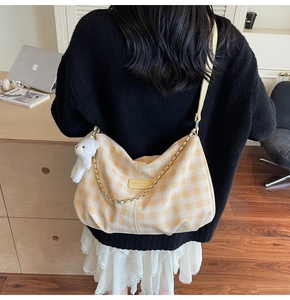 Detail of checkered crossbody bag with plush bear charm and chain strap on a model