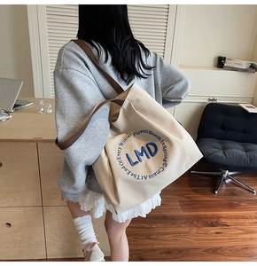 Close-up of model carrying canvas tote with blue embroidery and brown straps