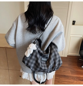Detail of grey plaid tote bag with chain strap and white plush bear pendant accessory