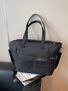 Grand sac fourre-tout en nylon noir avec bandoulière réglable sur un fauteuil en cuir noir