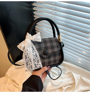 Detail of checkered square handbag featuring white lace bow and large black circular handle