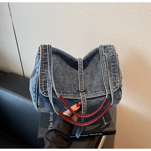 Detail of vintage denim shoulder bag with red leather handles and metal clasp buckle