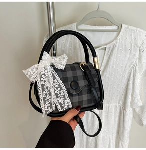 Detail of grey plaid handbag with black buckle and white lace bow decoration