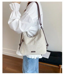 Detail of off-white canvas tote with brown leather strap and metal logo plaque