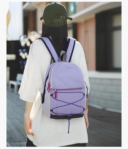 Outdoor back view of a lightweight light purple nylon backpack with blue elastic cords