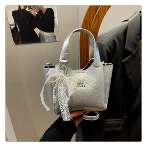 Detailed shot of a textured silver bucket bag featuring pearl and lace bow charm