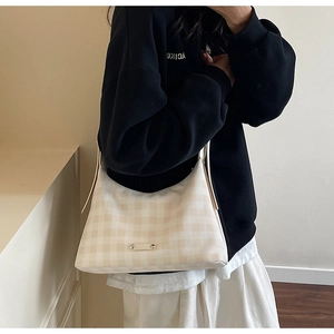 Détail du sac hobo à carreaux crème avec plaque logo argentée et bandoulière longue