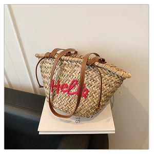 Détail d'un sac cabas en paille tressée avec broderie Hello rose et anses en cuir