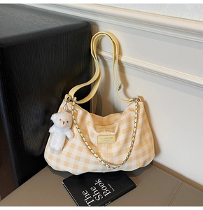 Detail of yellow plaid tote bag featuring a leather logo patch and a plush bear charm