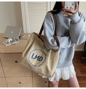 Detail of canvas tote bag with LMD embroidery and brown leather straps in a lifestyle setting