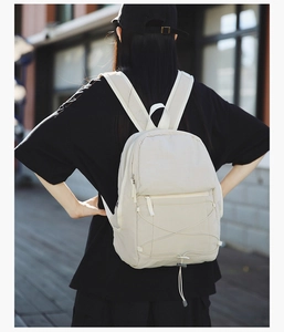Outdoor view of a lightweight beige backpack featuring functional crisscross bungee cords