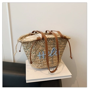 Détail du sac seau en paille avec broderie Hello bleue et bandoulières en cuir
