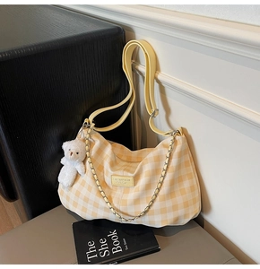 Detail of yellow checkered shoulder bag with plush bear charm and chain strap
