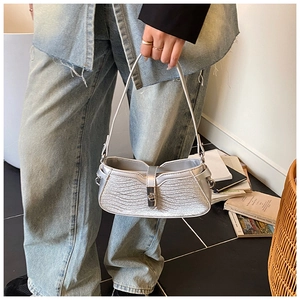 Detail of silver metallic shoulder bag featuring wavy stitching and a metal buckle closure