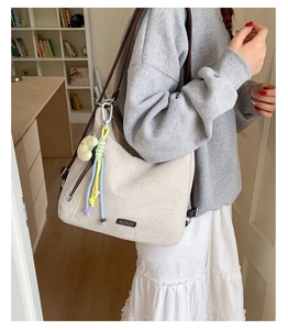 Detail of beige canvas tote bag with brown straps, colorful tassels and plush pendant
