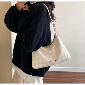 Détail du sac hobo à carreaux avec plaque logo métallique et texture en toile crème