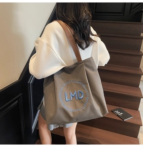 Detail of canvas tote bag with LMD embroidery and brown leather straps on model