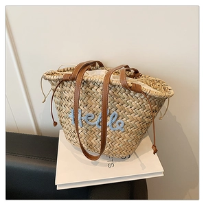 Détail d'un sac cabas en paille avec broderie Hello bleue et anses en cuir