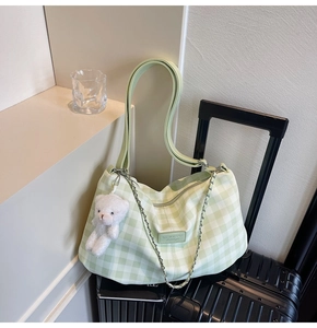 Detail of green plaid hobo bag featuring a plush bear pendant and metal chain accessory