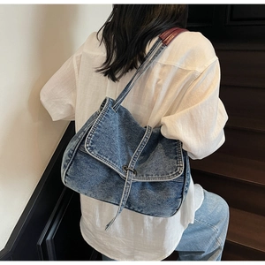 Blue denim crossbody bag with burgundy strap worn by model on minimalist stairs