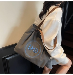 Detail of grey canvas tote bag with blue letter embroidery and brown wide shoulder straps