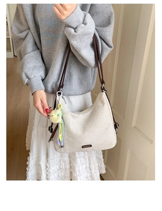 Detail of a beige canvas shoulder bag with brown straps and a cute cartoon charm