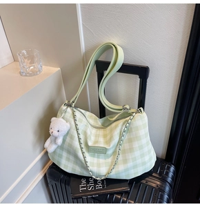 Detail of green gingham tote bag with wide strap, silver chain and plush bear charm