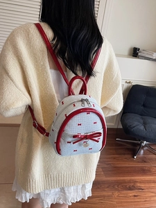 Mini preppy style cream backpack with red bow prints and heart pendant shown on model