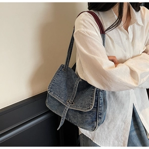 Close-up of blue washed denim shoulder bag with flap cover and metallic buckle detail